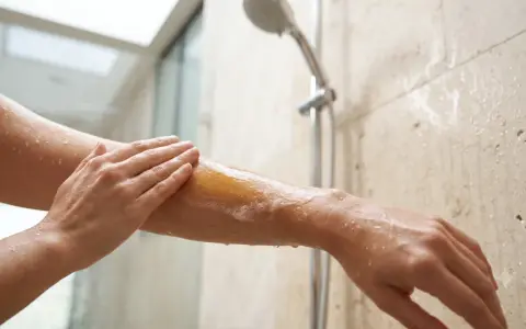 Une main applique du lait de douche moussant sur un bras sous la douche. C'est quoi le lait de douche ? Une expérience hydratante.
