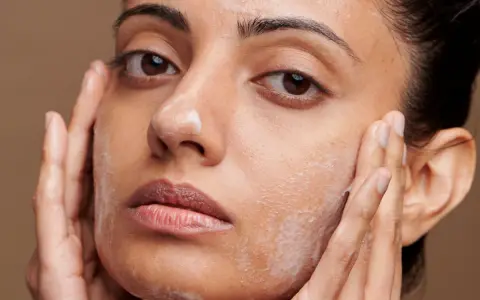Une femme applique un nettoyant moussant sur son visage, suivant un protocole soin visage. Ses mains massent doucement sa peau.