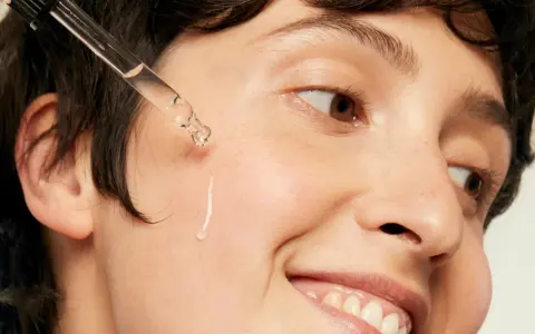 Une goutte d'acide hyaluronique tombe sur la joue d'une personne souriante, une solution pour l'hydratation et la lutte contre l'acné.