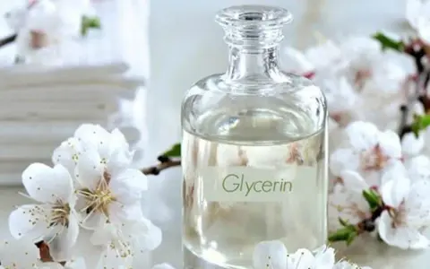 Bouteille de glycérine entourée de fleurs blanches. Attention, la glycérine peut présenter un danger si mal utilisée.