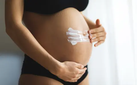 Ventre d'une femme enceinte recevant une crème hydratante. L'acide glycolique est souvent déconseillé pendant la grossesse.