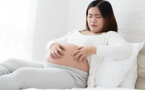 Femme enceinte se grattant le ventre, visiblement gênée par une peau sèche pendant la grossesse.