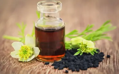 Flacon d'huile de nigelle, graines noires et fleurs sur fond de bois. Attention, l'huile de nigelle peut être dangereuse si mal utilisée.