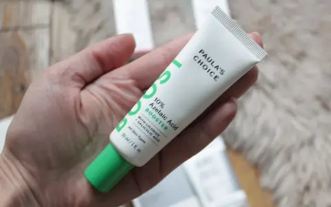 Tube de Paula's Choice 10% Azelaic Acid Booster, contenant de l'acide azélaïque et de la vitamine C, tenu dans une main.