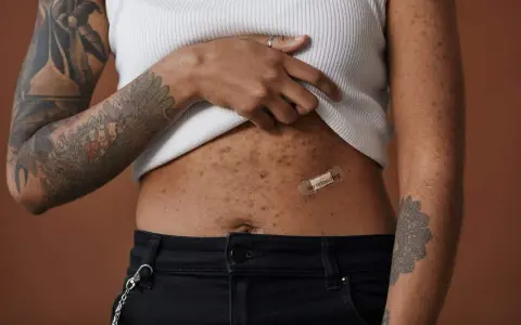 Une femme montre sa peau après accouchement, marquée par des taches et des tatouages. Un pansement "no retouching" sur son ventre célèbre l'authenticité.