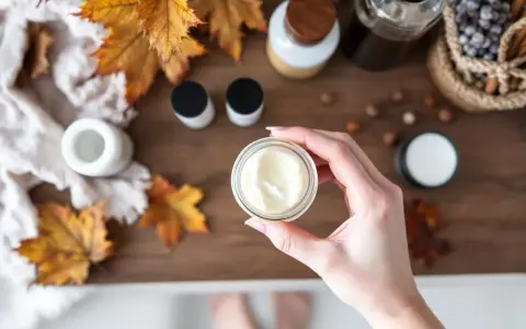 Maintenant, je ne veux plus mettre aucune crème sur ma peau. Une main tient un pot de crème, entouré de feuilles d'automne et de produits de soin.