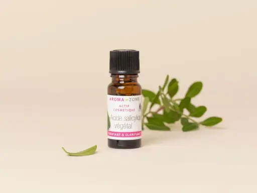 Flacon d'acide salicylique végétal Aroma-Zone, un actif cosmétique purifiant et clarifiant pour la peau, entouré de feuilles vertes.