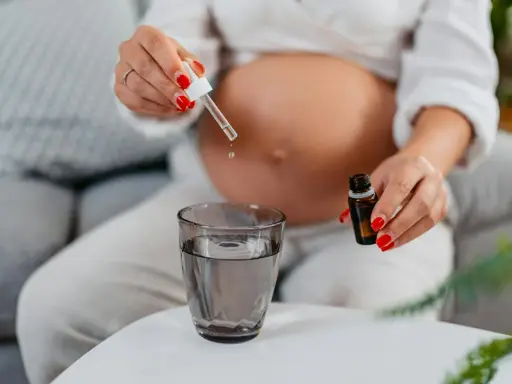 Une femme enceinte ajoute des gouttes d'huile essentielle dans un verre d'eau.