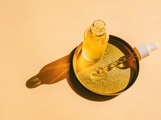 Flacon d'huile de tsubaki doré sur un plateau, avec une pipette prête à délivrer ses bienfaits.