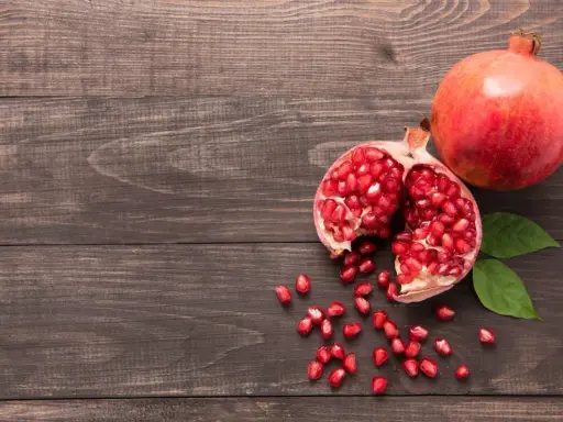 Grenade entière et ouverte, révélant ses arilles rouges. Un fruit aux multiples bienfaits pour la peau, posé sur un fond de bois sombre.