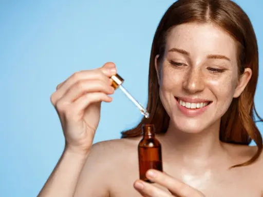 Femme rousse souriante appliquant un sérum. Attention au tocophérol danger potentiel dans certains produits.