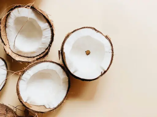 Plusieurs moitiés de noix de coco fraîches sur fond beige. Un aperçu des bienfaits de l'huile de coco.