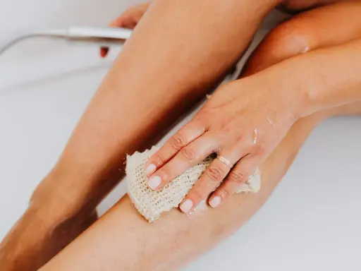 Main d'une femme utilisant une éponge pour exfolier sa peau douce et soyeuse dans la baignoire.