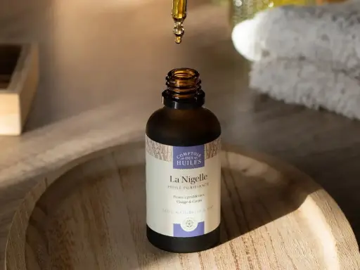 Goutte d'huile de nigelle purifiante tombant dans un flacon, idéale pour l'acné et les peaux à problèmes.