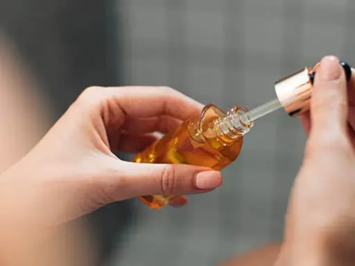 Mains de femme tenant un flacon compte-gouttes d'huile dorée, attention au danger du niacinamide mal utilisé.
