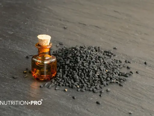 Huile de nigelle dans un flacon, à côté d'une pile de graines noires. Découvrez comment utiliser l'huile de nigelle pour ses bienfaits.