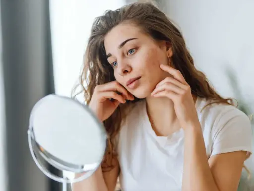 Jeune femme examinant un bouton sur sa joue, se demandant si le dentifrice pourrait aider.