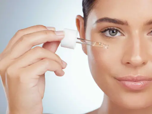 Une main applique une goutte de sérum sur le visage. Apprenez comment utiliser le rétinol pour une peau éclatante.