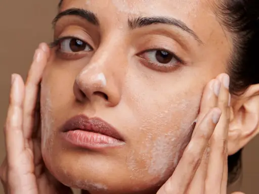 Une femme applique un nettoyant moussant sur son visage, suivant un protocole soin visage. Ses mains massent doucement sa peau.