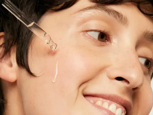 Une goutte d'acide hyaluronique tombe sur la joue d'une personne souriante, une solution pour l'hydratation et la lutte contre l'acné.