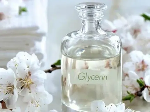 Bouteille de glycérine entourée de fleurs blanches. Attention, la glycérine peut présenter un danger si mal utilisée.