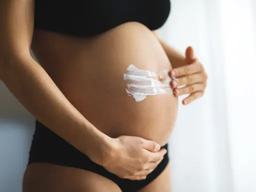Ventre d'une femme enceinte recevant une crème hydratante. L'acide glycolique est souvent déconseillé pendant la grossesse.