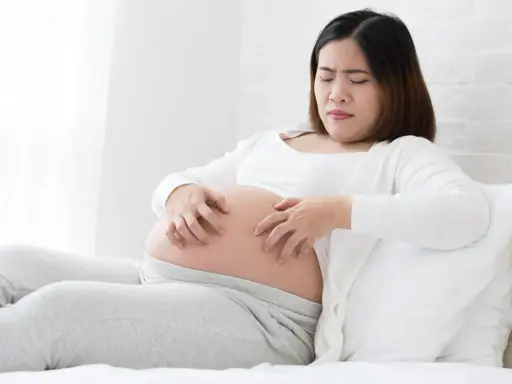 Femme enceinte se grattant le ventre, visiblement gênée par une peau sèche pendant la grossesse.