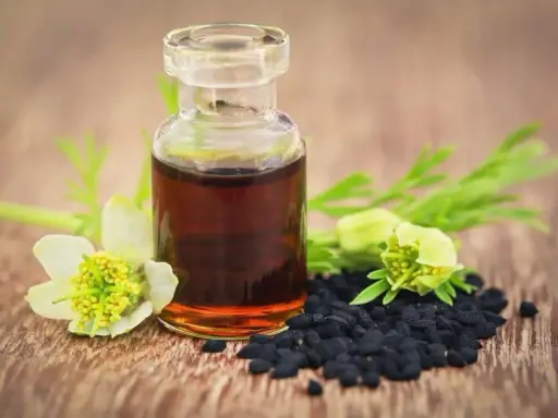 Flacon d'huile de nigelle, graines noires et fleurs sur fond de bois. Attention, l'huile de nigelle peut être dangereuse si mal utilisée.