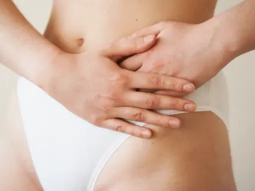 Mains sur le ventre, une femme porte une culotte blanche. Une légère plaque rouge est visible sur son pubis.