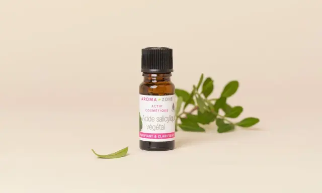 Flacon d'acide salicylique végétal Aroma-Zone, un actif cosmétique purifiant et clarifiant pour la peau, entouré de feuilles vertes.