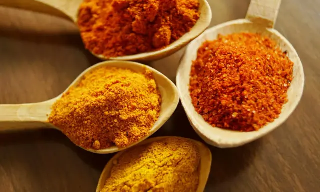 Cuillères en bois remplies d'épices colorées, dont le curcuma, parfait pour la peau.