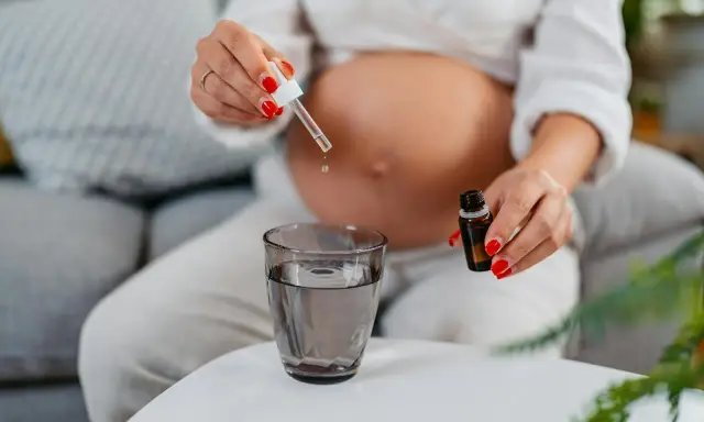 Une femme enceinte ajoute des gouttes d'huile essentielle dans un verre d'eau.