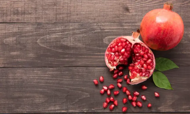 Grenade entière et ouverte, révélant ses arilles rouges. Un fruit aux multiples bienfaits pour la peau, posé sur un fond de bois sombre.