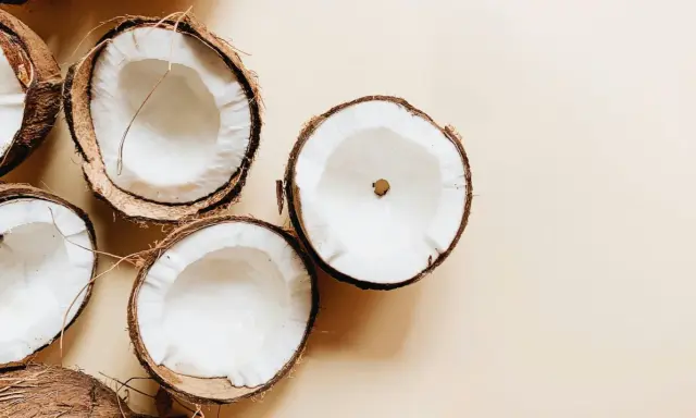 Plusieurs moitiés de noix de coco fraîches sur fond beige. Un aperçu des bienfaits de l'huile de coco.