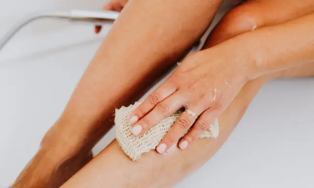 Main d'une femme utilisant une éponge pour exfolier sa peau douce et soyeuse dans la baignoire.