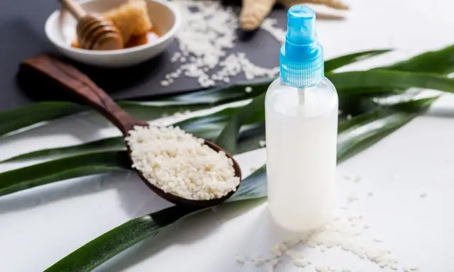 Bouteille de spray contenant de l'eau de riz pour le visage, avec une cuillère de riz et du miel en arrière-plan.