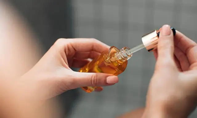 Mains de femme tenant un flacon compte-gouttes d'huile dorée, attention au danger du niacinamide mal utilisé.