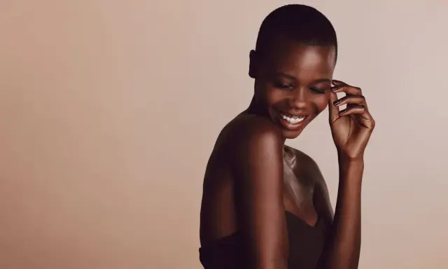 Une femme rit, sa peau foncée, riche en mélanine, le pigment responsable de la couleur de la peau, brille sous la lumière.