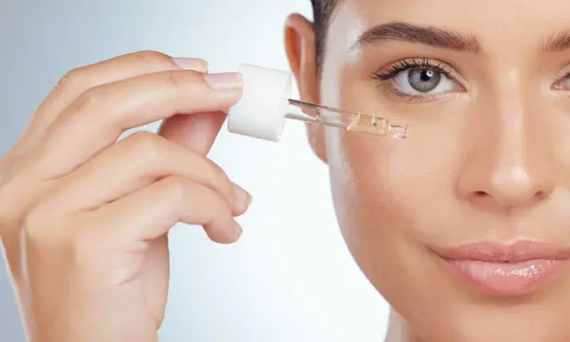 Une main applique une goutte de sérum sur le visage. Apprenez comment utiliser le rétinol pour une peau éclatante.
