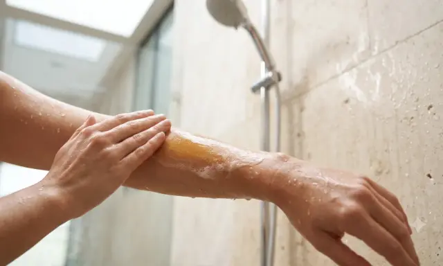 Une main applique du lait de douche moussant sur un bras sous la douche. C'est quoi le lait de douche ? Une expérience hydratante.