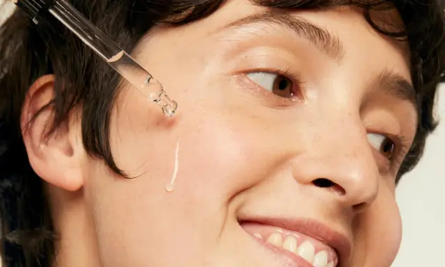 Une goutte d'acide hyaluronique tombe sur la joue d'une personne souriante, une solution pour l'hydratation et la lutte contre l'acné.