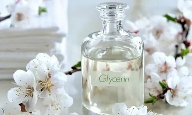 Bouteille de glycérine entourée de fleurs blanches. Attention, la glycérine peut présenter un danger si mal utilisée.