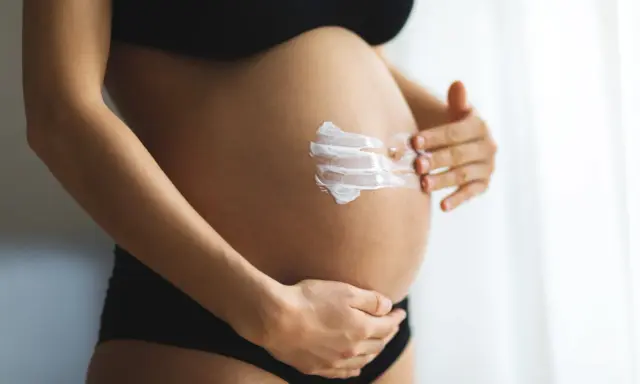 Ventre d'une femme enceinte recevant une crème hydratante. L'acide glycolique est souvent déconseillé pendant la grossesse.