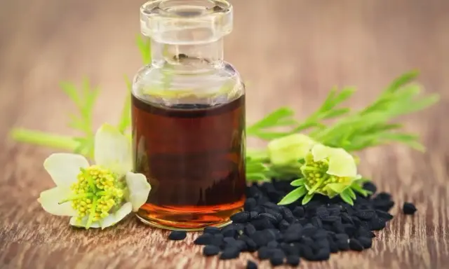 Flacon d'huile de nigelle, graines noires et fleurs sur fond de bois. Attention, l'huile de nigelle peut être dangereuse si mal utilisée.