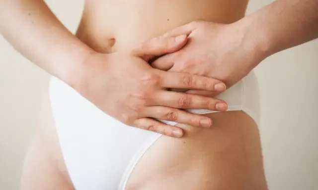 Mains sur le ventre, une femme porte une culotte blanche. Une légère plaque rouge est visible sur son pubis.