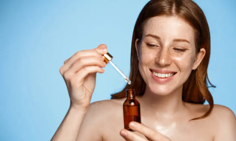 Femme rousse souriante appliquant un sérum. Attention au tocophérol danger potentiel dans certains produits.