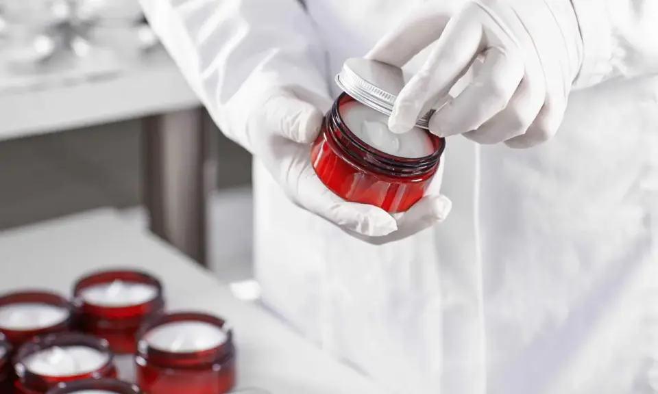 Mains gantées ouvrant un pot de crème cosmétique. Le polysorbate 60 est un ingrédient clé pour sa texture.