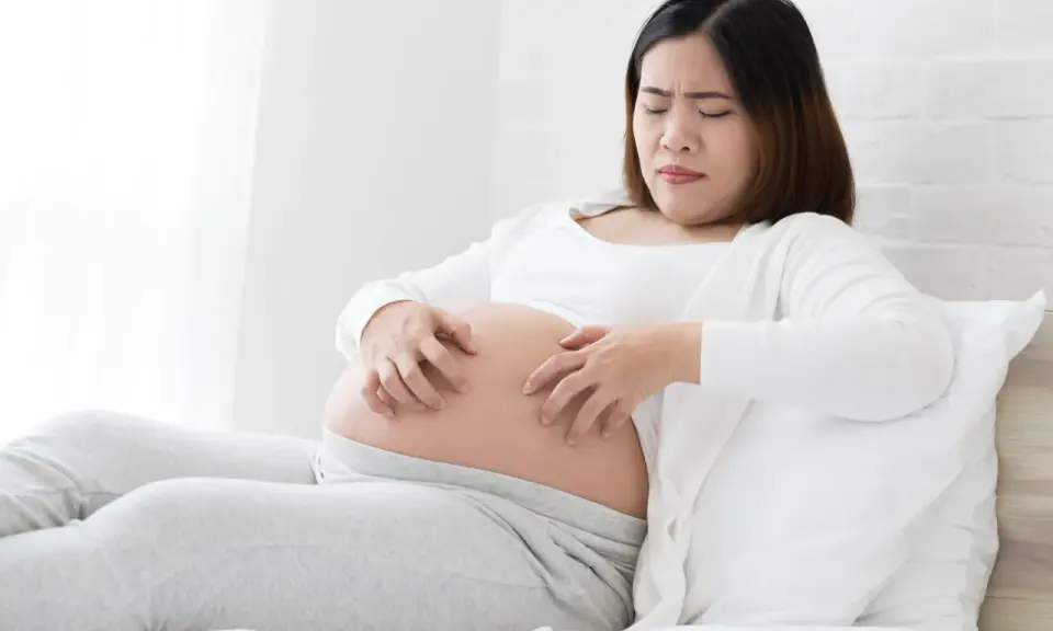 Femme enceinte se grattant le ventre, visiblement gênée par une peau sèche pendant la grossesse.