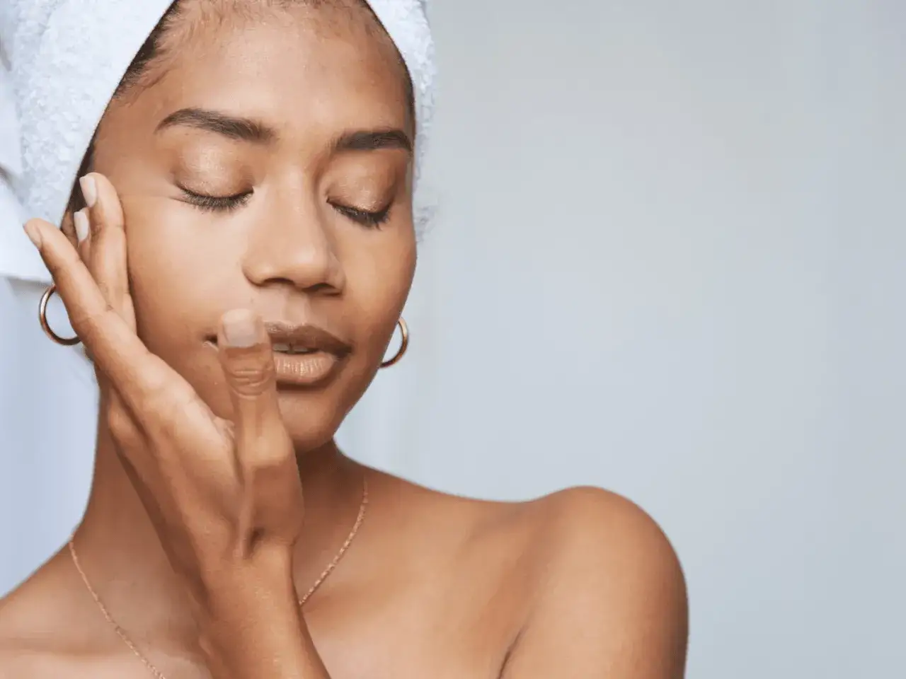 Une femme aux yeux ferm&eacute;s, une serviette sur la t&ecirc;te, caresse son visage. Elle profite d'un moment pour exfolier sa peau.