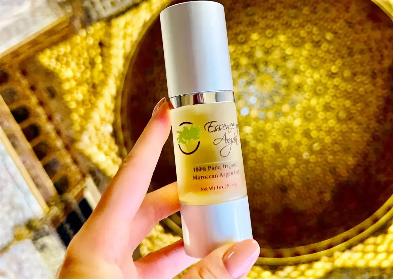 Main d'une femme tenant une bouteille d'huile d'argan bio. Bien que l'huile d'argan soit généralement sans effets secondaires, une utilisation excessive peut irriter la peau.